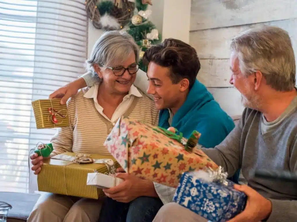 Gift ideas when retiring parents: adult son surprising mom and dad with wrapped presents during home celebration.