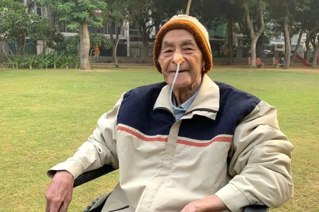 Elderly man undergoing stroke rehabilitation sits calmly in a garden, wearing a nasal feeding tube as part of his ongoing medical recovery and supportive care.