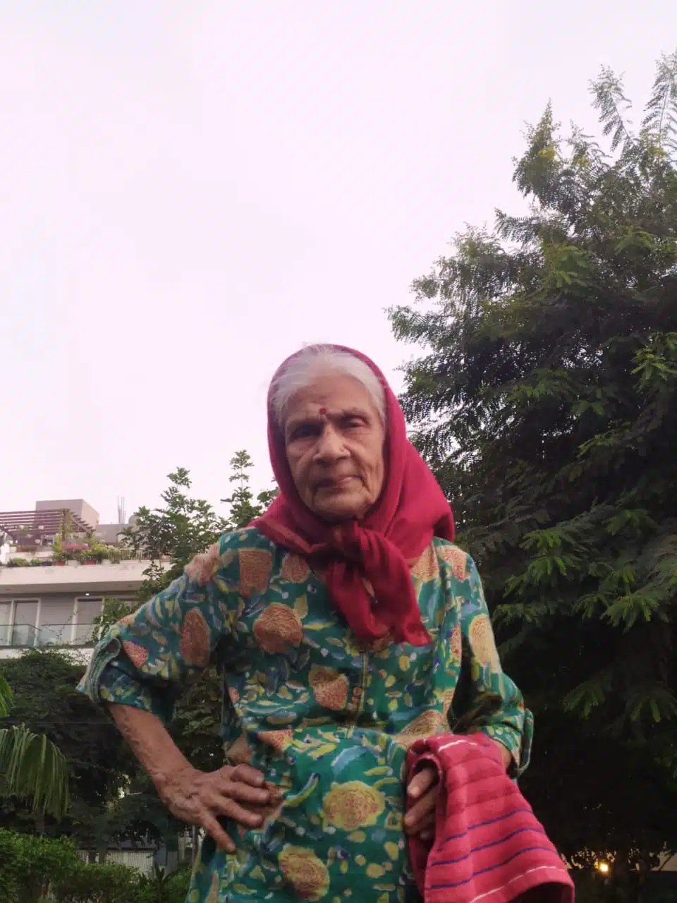 Elderly woman in a red dupatta sitting outdoors in a garden in winter, Gurgaon